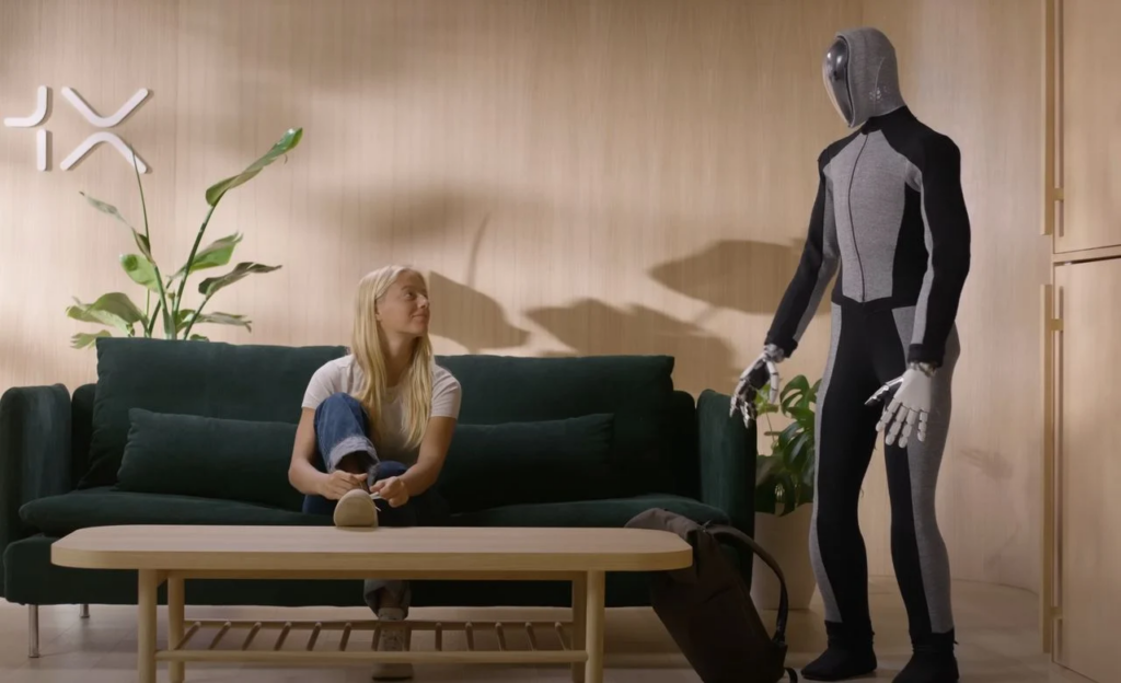 Una chica sentada en un sillón color verde oscuro mirando a un robot con forma humana parado a su derecha.